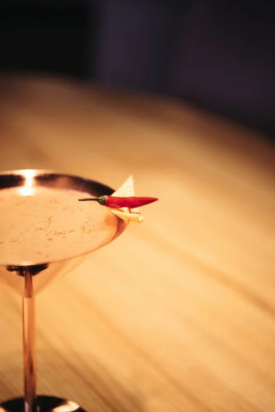 Вибірковий фокус алкогольного коктейлю в металевому склі, прикрашеному перцем чилі та чіпом на дерев'яному столі — стокове фото