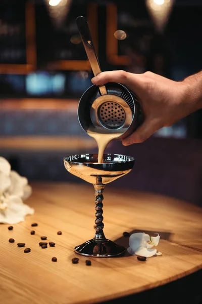 Barman versant cocktail de shaker à travers tamis en verre métallique sur table en bois — Photo de stock