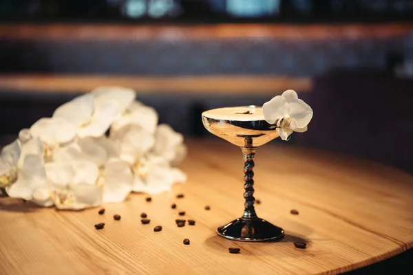 Foyer sélectif de cocktail alcoolisé en verre métallique décoré de fleurs d'orchidée et de grains de café sur fond sombre — Photo de stock