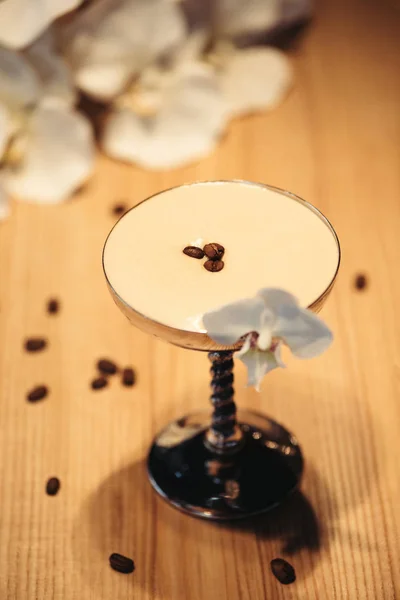 Cóctel alcohólico en vidrio de metal decorado con flores de orquídea y granos de café en mesa de madera - foto de stock