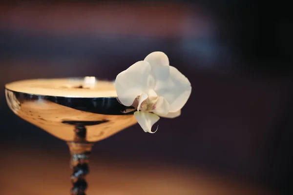 Primer plano de cóctel alcohólico en vidrio de metal decorado con flor de orquídea sobre fondo oscuro - foto de stock