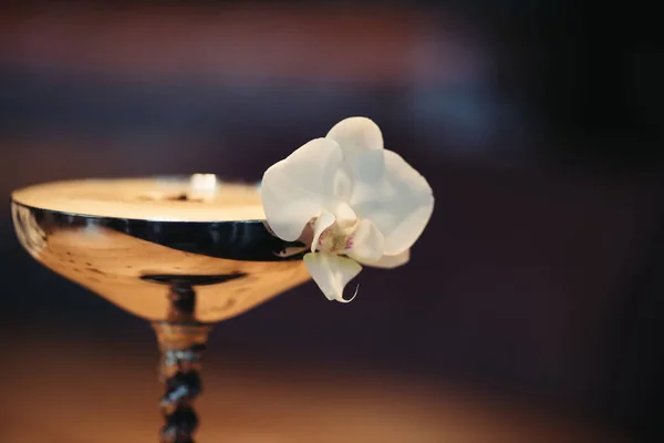 Gros plan de cocktail alcoolisé en verre métallique décoré de fleurs d'orchidée sur fond sombre — Photo de stock