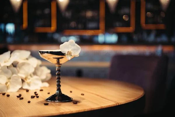 Cóctel alcohólico en vidrio de metal decorado con flores de orquídea y granos de café en mesa de madera - foto de stock