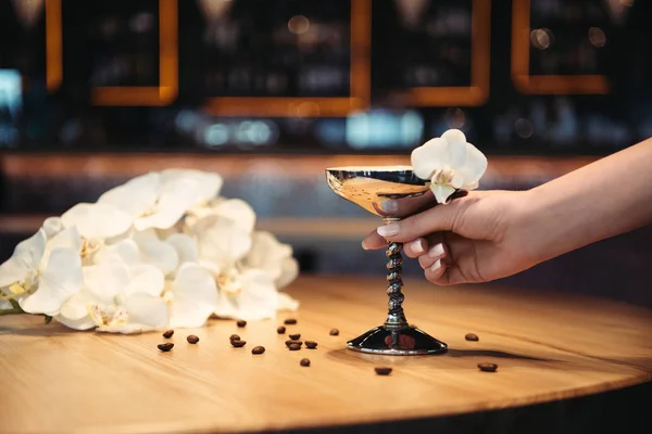 Cropped view of woman holding alcoholic cocktail in metal glass decorated with orchid flower and coffee beans — Stock Photo
