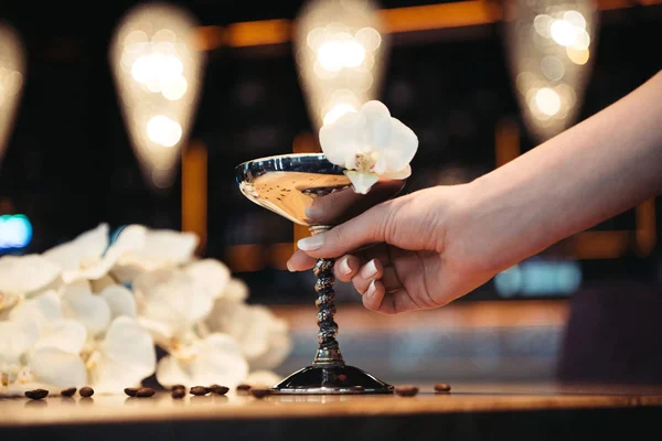 Abgeschnittene Ansicht einer Frau mit alkoholischem Cocktail in Metallglas mit Orchideenblume verziert — Stockfoto