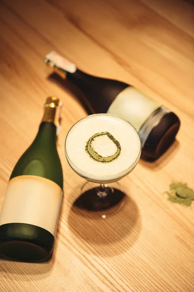 Delicioso coquetel com espuma na mesa de madeira com garrafas de champanhe no fundo — Fotografia de Stock