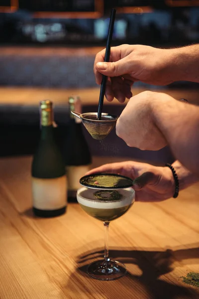 Vista parziale dei baristi che preparano cocktail alcolici utilizzando setaccio su tavolo di legno in bar — Foto stock