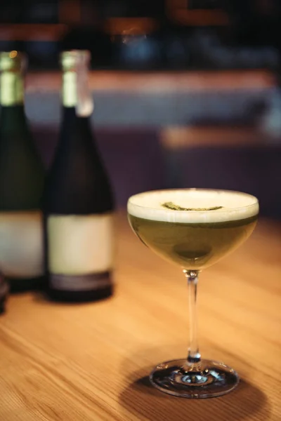 Selective focus of delicious cocktail with foam on wooden table and bottles of champagne on background — Stock Photo