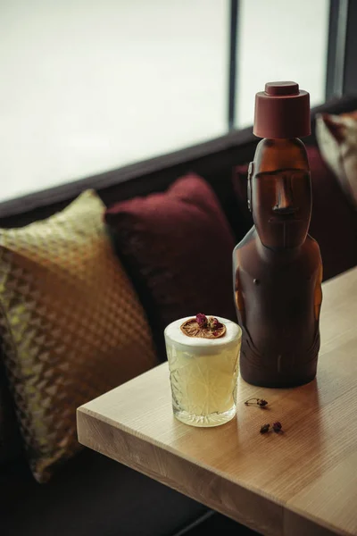 Estatua de bronce y cóctel alcohólico decorado con naranja seca en la mesa de madera en el restaurante - foto de stock