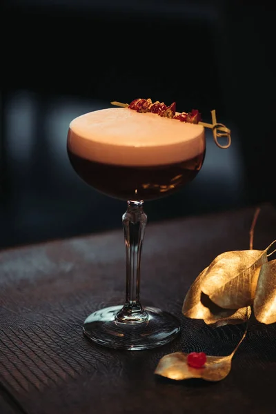 Селективный акцент алкогольного коктейля с пеной и сухими цветами на темном фоне — стоковое фото