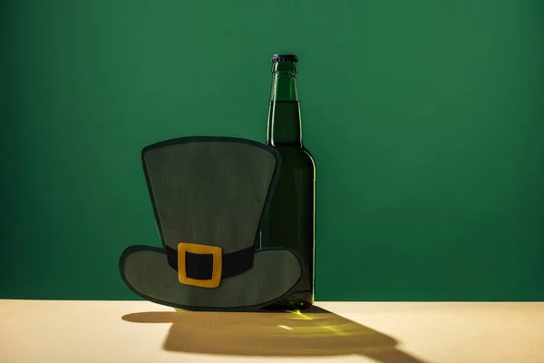 Bierflaschen und Papierhut isoliert auf grünem, st patrick day Konzept — Stockfoto