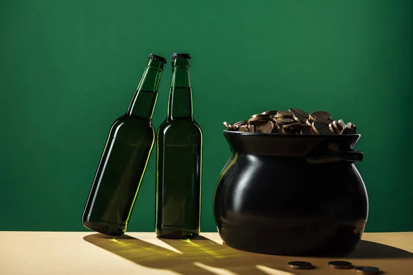 Beer bottles and black pot with golden coins isolated on green, st patrick day concept — Stock Photo