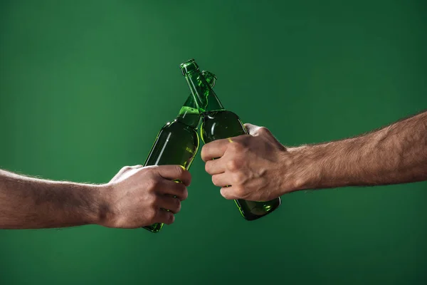 Visão parcial de homens clinking garrafas de cerveja isoladas em verde, st patrick conceito dia — Fotografia de Stock
