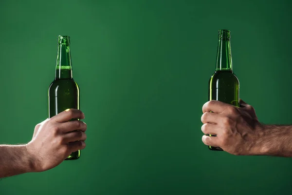 Обрізаний вид чоловіків, що тримають пляшки пива ізольовані на зеленому з копіювальним простором, концепція дня святого Патріка — стокове фото