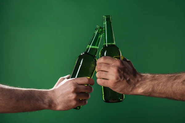 Vue recadrée des hommes clinquant des bouteilles de bière isolées sur vert, concept st patrick jour — Photo de stock