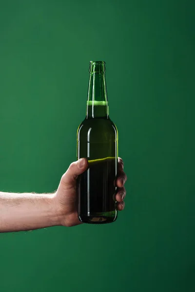 Обрізаний вид людини, що тримає пляшку пива ізольовано на зеленому, концепція дня святого Патріка — стокове фото