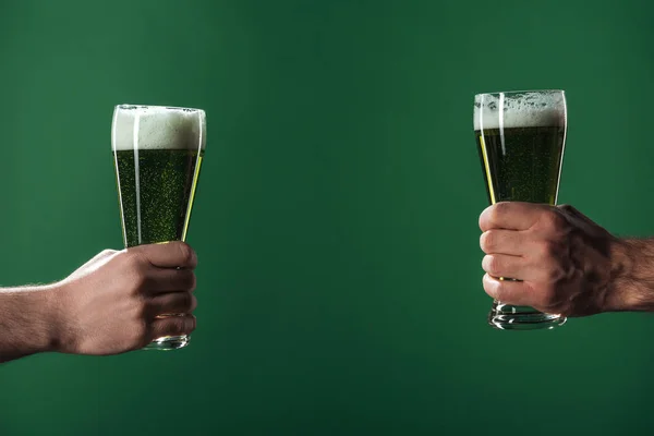 Cropped view of men holding glasses of beer with foam isolated on green, st patrick day concept — Stock Photo