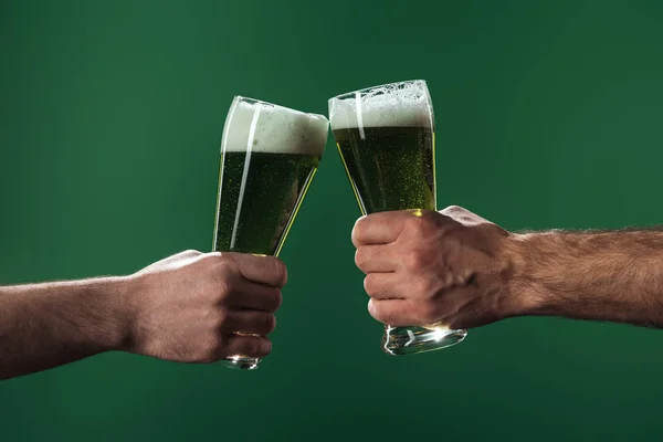 Abgeschnittene Ansicht von Männern, die Biergläser klappern, isoliert auf grünem, st patrick day Konzept — Stockfoto