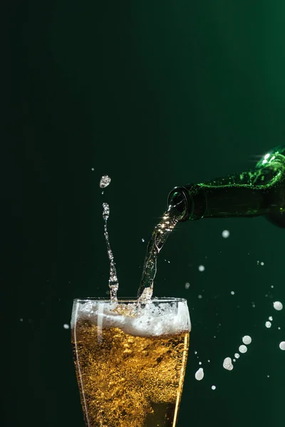 Наливая пиво в стекло с брызгами и копировальным пространством, изолированным на зеленой концепции Дня Святого Патрика — стоковое фото