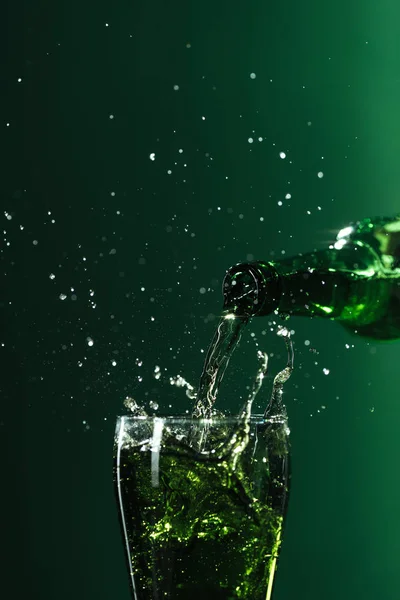 Лиття пива в склянку з бризками ізольовано на зеленому, концепція святкового дня — стокове фото