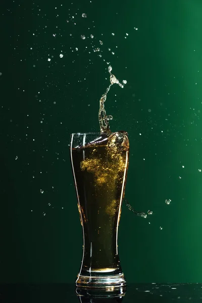 Склянка холодного пива з бризками ізольовано на зеленому, концепція дня святого Патріка — стокове фото