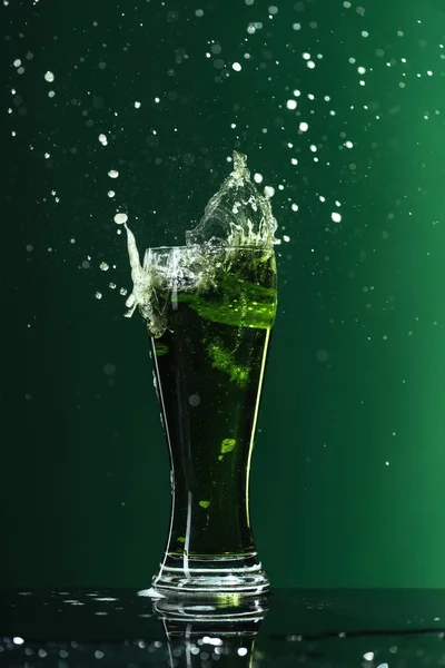 Verre de bière avec éclaboussures isolé sur vert, concept st patrick jour — Photo de stock