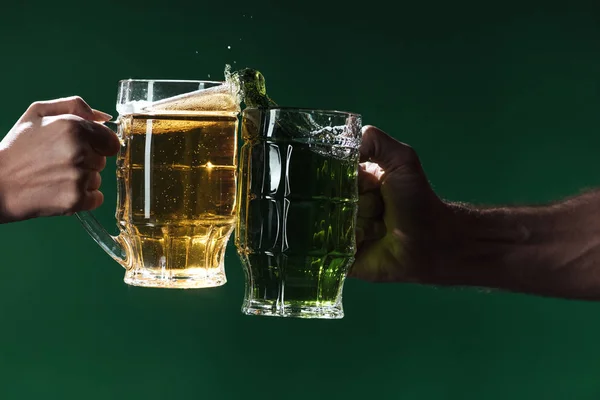 Teilansicht von Männern, die Biergläser mit Spritzern klappern, isoliert auf dunkelgrünem, patrick day Konzept — Stockfoto