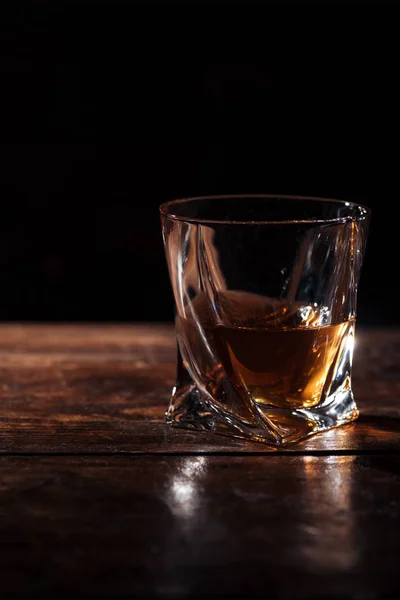 Close-up view of brandy in glass on wooden table on black — Stock Photo