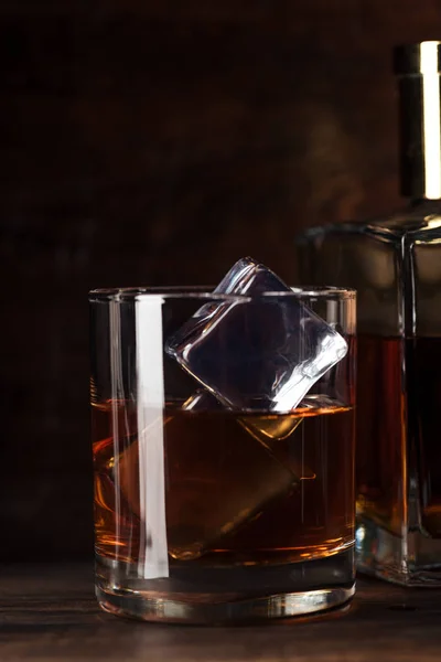 Vista de primer plano del vaso de bourbon con cubitos de hielo y botella sobre mesa de madera - foto de stock