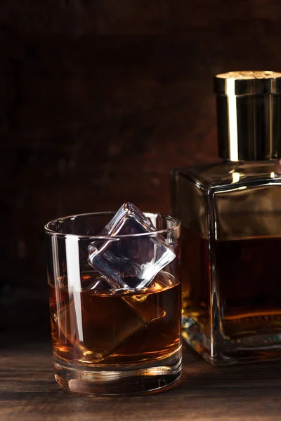 Close-up view of glass of cognac with ice cubes and bottle on wooden table — Stock Photo