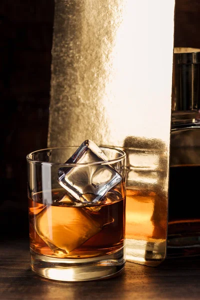 Close-up view of glass of amber alcohol with ice cubes on wooden table — Stock Photo