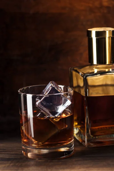 Vue rapprochée du verre de brandy avec glaçons et bouteille sur table en bois — Photo de stock