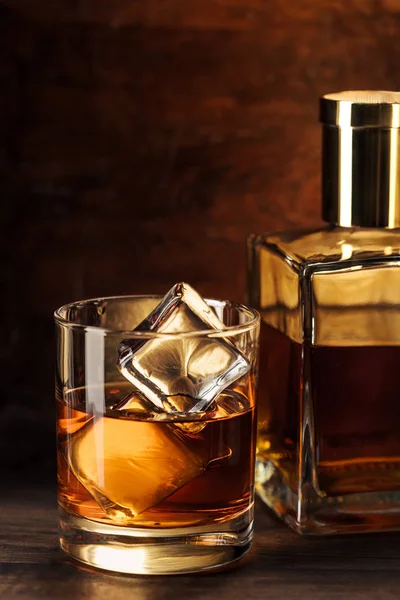 Nahaufnahme eines Whiskyglases mit Eiswürfeln und Flasche auf Holztisch — Stockfoto