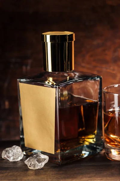 Close-up view of whiskey bottle with blank label, ice cubes and glass on wooden table — Stock Photo