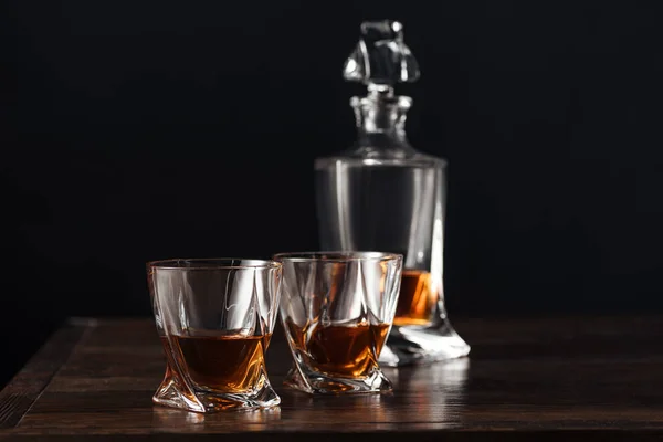 Vista de cerca de vasos y botella de whisky sobre mesa de madera oscura aislada en negro - foto de stock