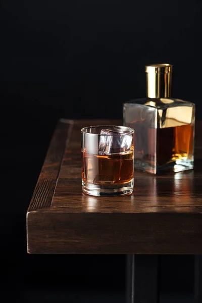 Vue rapprochée du verre et de la bouteille de whisky sur une table en bois sombre isolée sur fond noir — Photo de stock