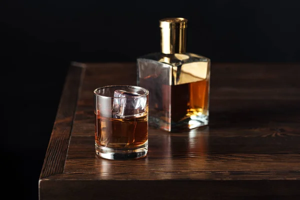 Vaso y botella de whisky sobre mesa de madera oscura aislada sobre negro - foto de stock