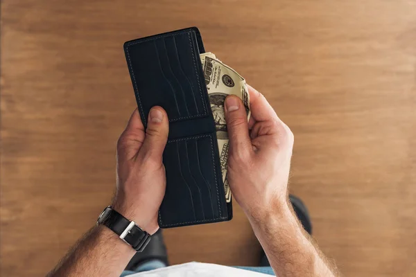 Вид зверху людини, що кладе доларові банкноти в гаманець на дерев'яному фоні — стокове фото