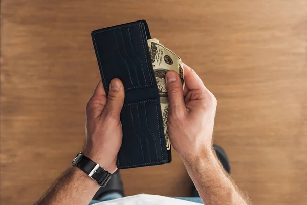 Vista superior del hombre puting billetes de dólares en cartera sobre fondo de madera - foto de stock