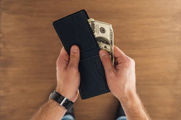 Vista superior del hombre puting billetes de dólares en cartera sobre fondo de madera - foto de stock