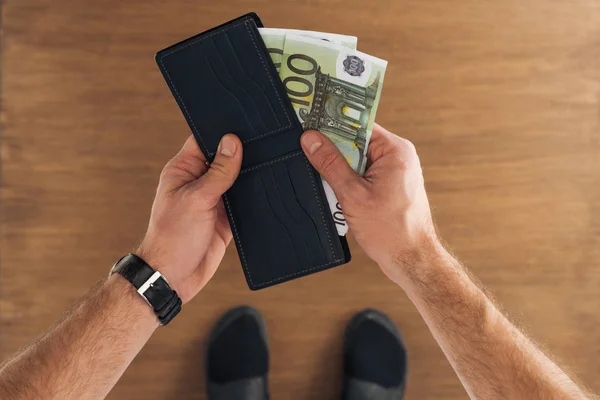 Top view of man puting euros banknotes in wallet on wooden background — Stock Photo