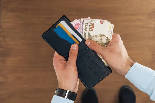 Top view of man taking from wallet with credit cards hryvnyas banknotes on wooden background — Stock Photo