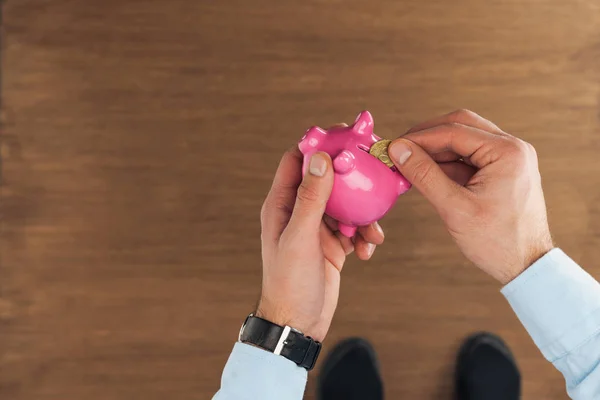 Top view of man puting in piggy bank coin on wooden background — Stock Photo