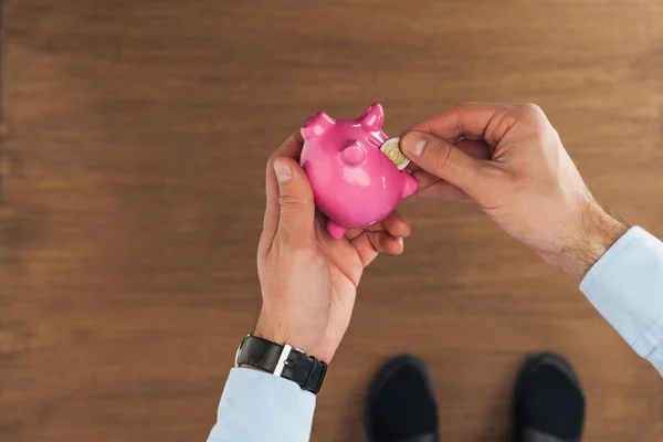 Cropped view of man puting in piggy bank coin on wooden background — Stock Photo