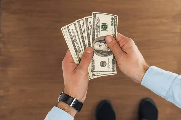 Vista superior del hombre sosteniendo billetes en dólares sobre fondo de madera - foto de stock