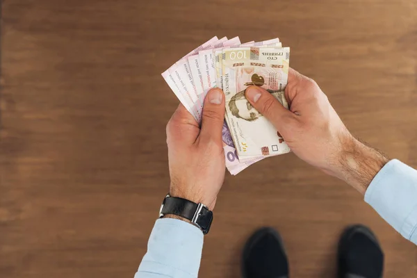 Top view of man holding hryvnias banknotes on wooden background — Stock Photo