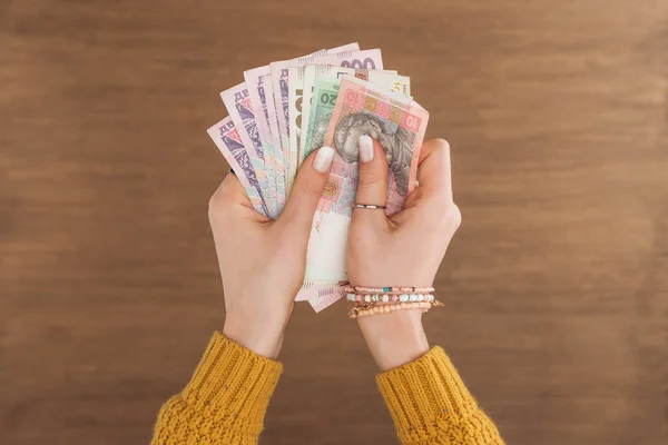 Vista superior de la mujer sosteniendo billetes de hryvnias sobre fondo de madera - foto de stock