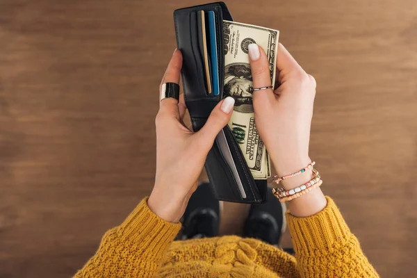 Vista superior de la mujer tomando billetes en dólares de billetera sobre fondo de madera - foto de stock