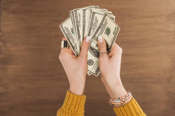 Vista superior de la mujer sosteniendo billetes en dólares sobre fondo de madera - foto de stock