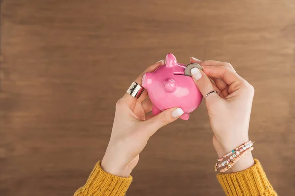 Top view of woman puting in pink piggy bank coin on wooden background — Stock Photo